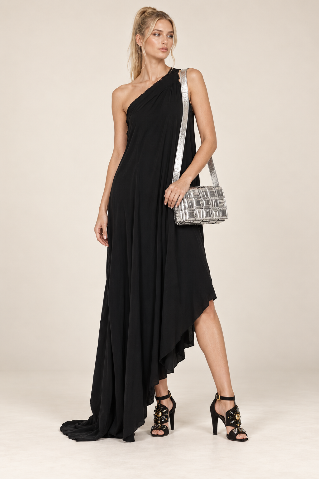 Blonde model in black Balenciaga one-shoulder dress with silver Bottega Veneta Cassette and Louis Vuitton sandals